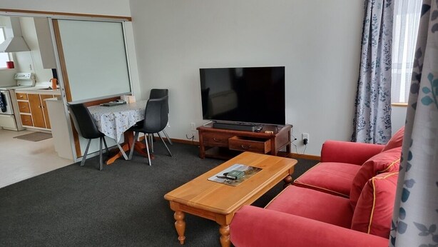 Ett vardagsrum med en röd soffa, ett träbord som används som soffbord, en tv och en matplats med ett bord och stolar.