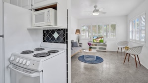 A kitchen with a white stove, microwave, and cabinets, a gray sofa, a TV, and a ceiling fan.