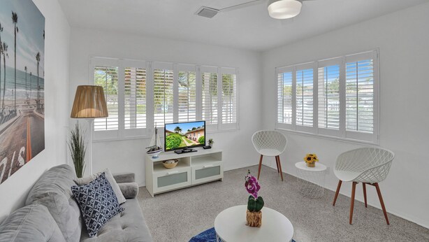 A modern living room with a white sofa, a TV on a white cabinet, two white chairs, and a ceiling fan.