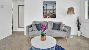 A modern living room with a grey sofa, a round coffee table with a plant, and a beach-themed artwork on the wall.
