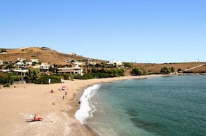 Une zone côtière avec une plage, une colline parsemée de bâtiments et un ciel dégagé.