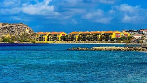A coastal hotel with multiple yellow buildings, a rocky cliff, and a clear blue sea.