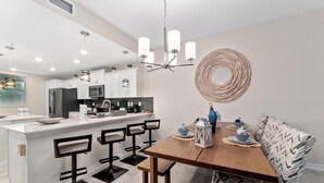 A modern kitchen with white cabinetry, a wooden dining table, and black bar stools. - Resort apartment in Kissimmee (Kissimmee)