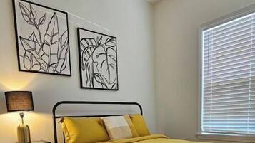 A bedroom with a bed, a nightstand, a lamp, and two wall art pieces.