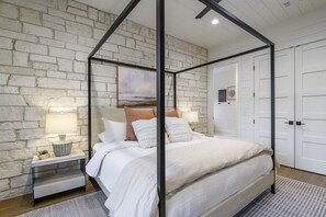 Uma cama de dossel com cabeceira branca, uma mesinha de cabeceira com abajur, e um painel de parede de pedra.
