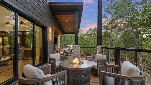 A wooden deck with outdoor furniture, a fire pit, and a stone fireplace.
