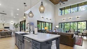 A spacious kitchen with a large island, modern pendant lights, and large windows offering a view of the outdoors.