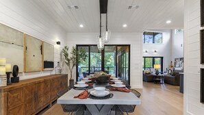 A spacious dining area with a long table, wooden cabinets, and a view of the outdoors.
