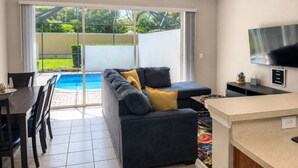 Una sala de estar moderna con un sofá, televisor y vista a la piscina.
