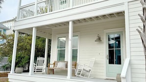 A two-story white house with a covered porch, a front door, and a small garden area. - Amazing Moonlight Escape- (Panama City Beach)