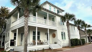 A two-story white house with a balcony, palm trees, and a brick driveway. - Amazing Moonlight Escape- (Panama City Beach)