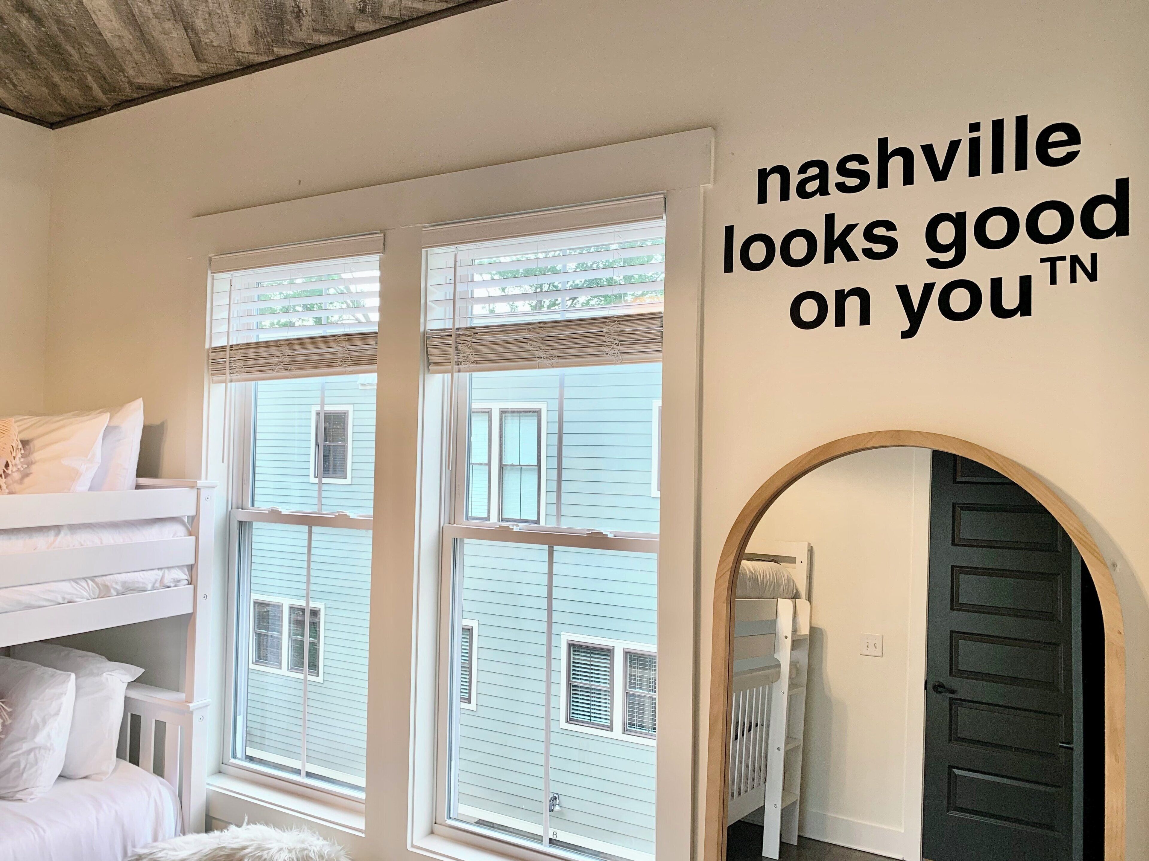 Een slaapkamer met stapelbedden, grote ramen en een bordje met de tekst 'Nashville staat jou goed'.