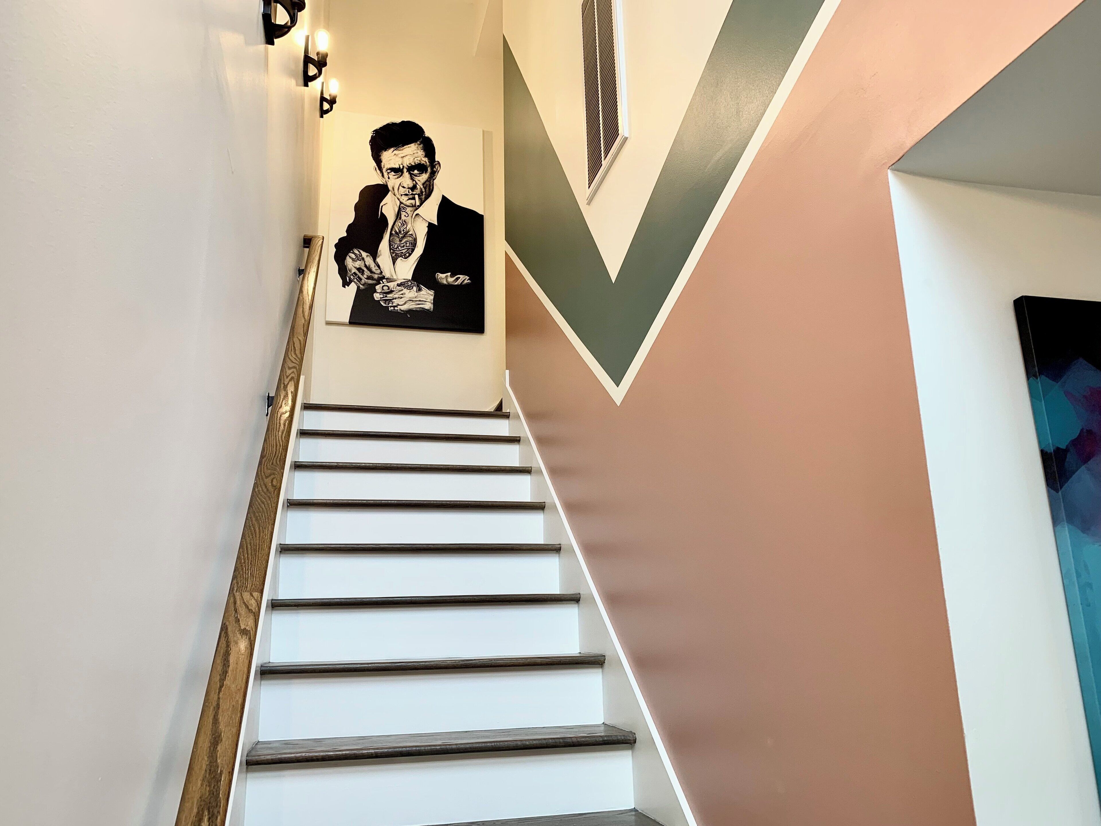 A staircase with a modern design, featuring a wooden handrail and white steps. A black and white portrait is displayed on the wall above the stairs.