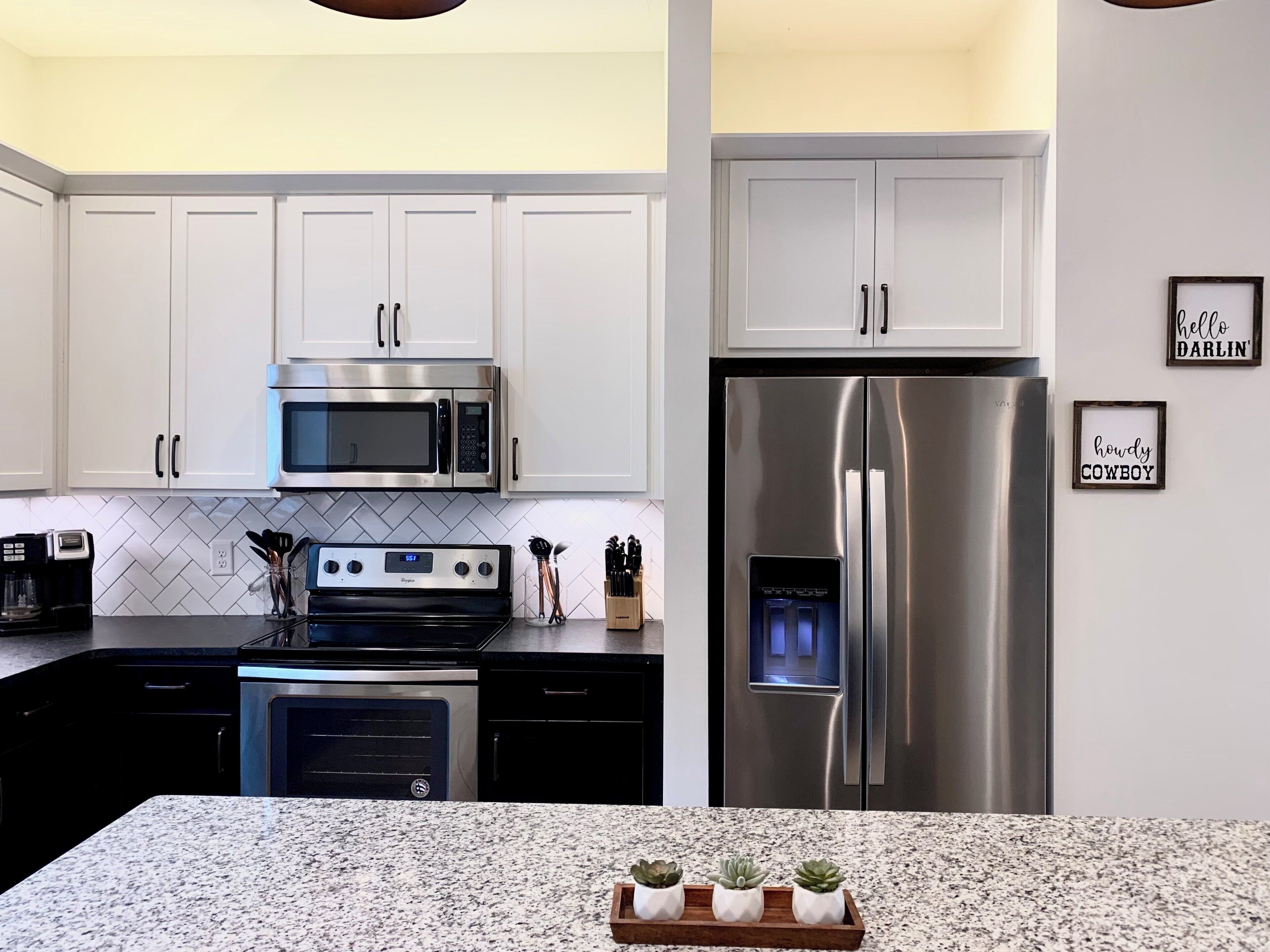 A modern kitchen with white cabinets, a stainless steel refrigerator, a microwave, and a dishwasher.