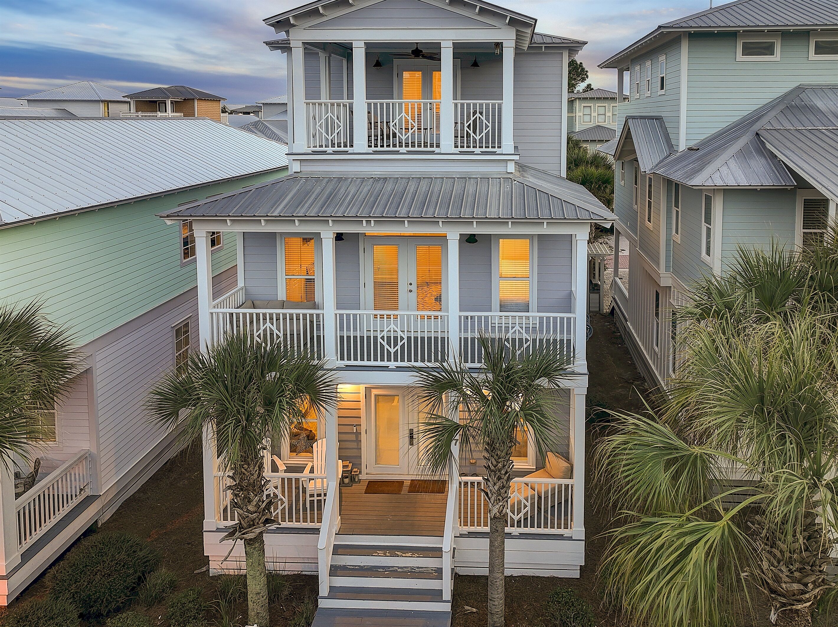 A two-story house with a balcony, a front porch, and a small garden area with palm trees.
