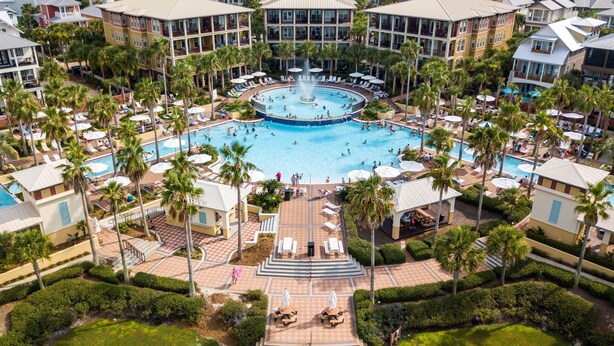Un resort con piscina central rodeada de palmeras y sillas de descanso.