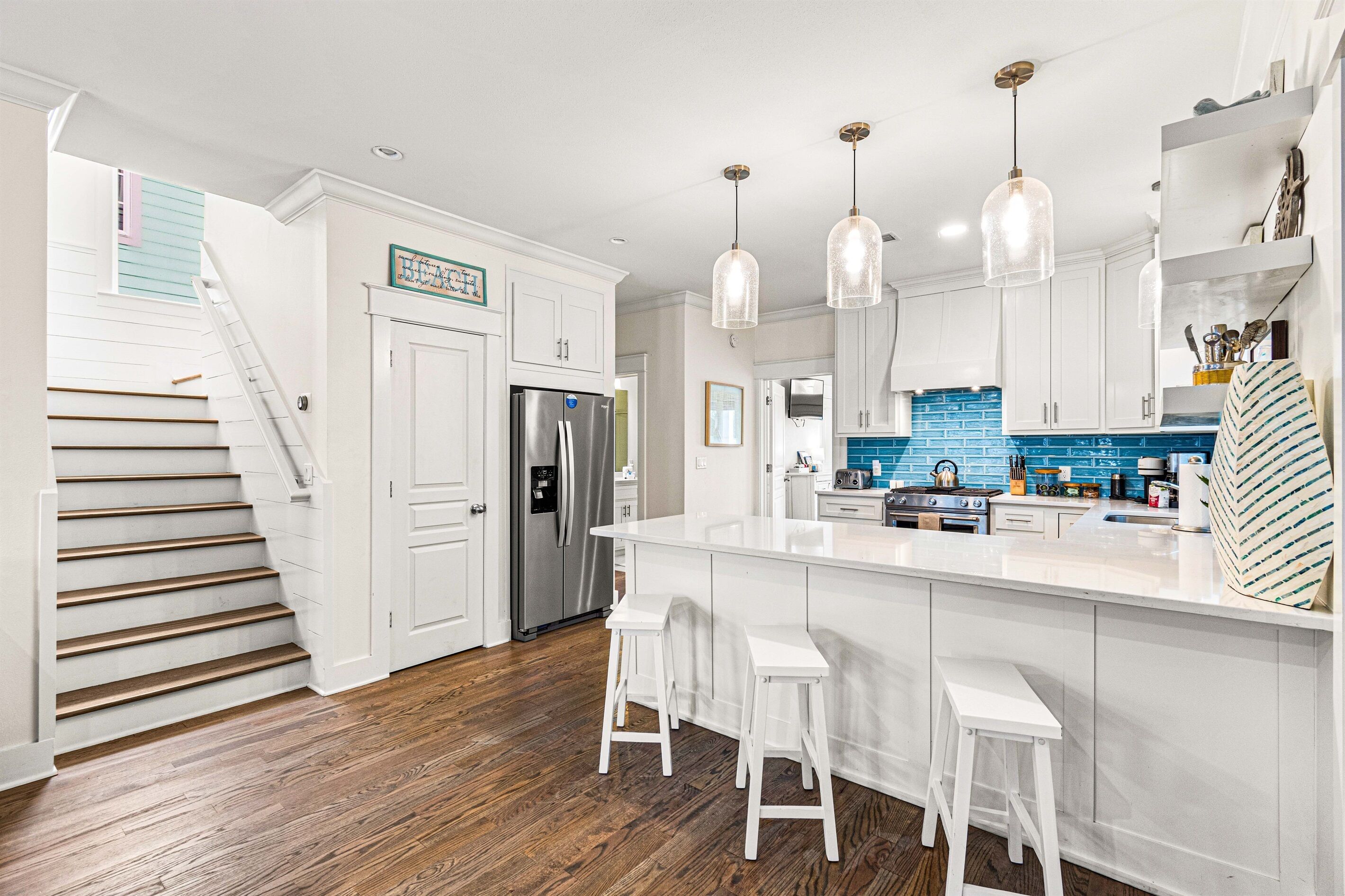 A modern kitchen with white cabinetry, a stainless steel refrigerator, a blue backsplash, and a large island with bar stools.