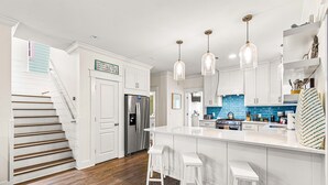 Una cocina moderna con armarios blancos, un refrigerador de acero inoxidable, un salpicadero azul y una isla grande con taburetes de bar.