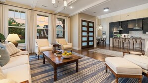 A spacious living room with a large window, a dining area, and a kitchen with dark cabinets and pendant lighting. - Modern Farmhouse steps from Momentary and MTB Trails. (Bentonville)