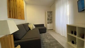 A modern living room with a sectional sofa, a wooden accent wall, a white shelving unit, and a grey rug. - Urban 44 Guest House<br> (Ponta Delgada)