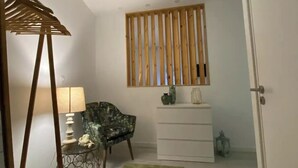A hallway with a wooden slat partition, a green rug, a chair, a small table with a lamp, and a white dresser. - Urban 44 Guest House<br> (Ponta Delgada)