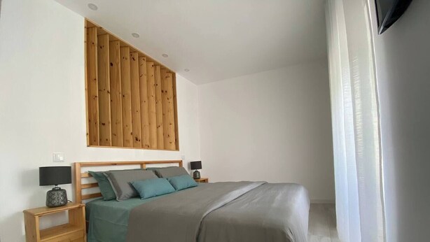 A bedroom with a bed, wooden headboard, nightstands, and a window with curtains. - Urban 44 Guest House<br> (Ponta Delgada)