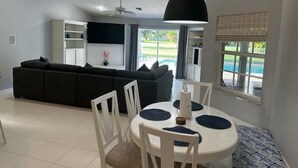 Ein modernes Wohnzimmer mit einer schwarzen Couch, einem weißen Esstisch mit Stühlen und einem Deckenventilator.
