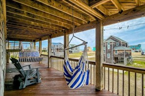 A wooden deck with a hammock and chairs, overlooking a beach with houses.