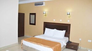 A hotel room with a large bed, a nightstand, two wall-mounted lamps, and an air conditioning unit. - Chilla Luxury Suites Kano (Kano)
