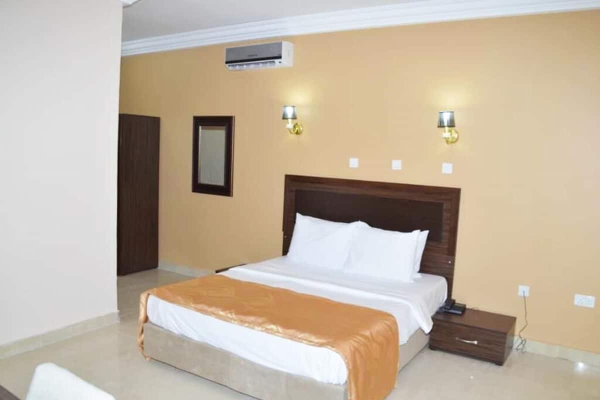 Une chambre d’hôtel avec un grand lit, une table de chevet, deux lampes fixées au mur et un appareil de climatisation.