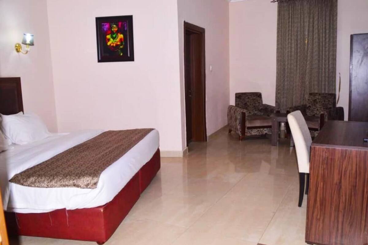 Une chambre d’hôtel avec un lit, un bureau, deux chaises et une porte.