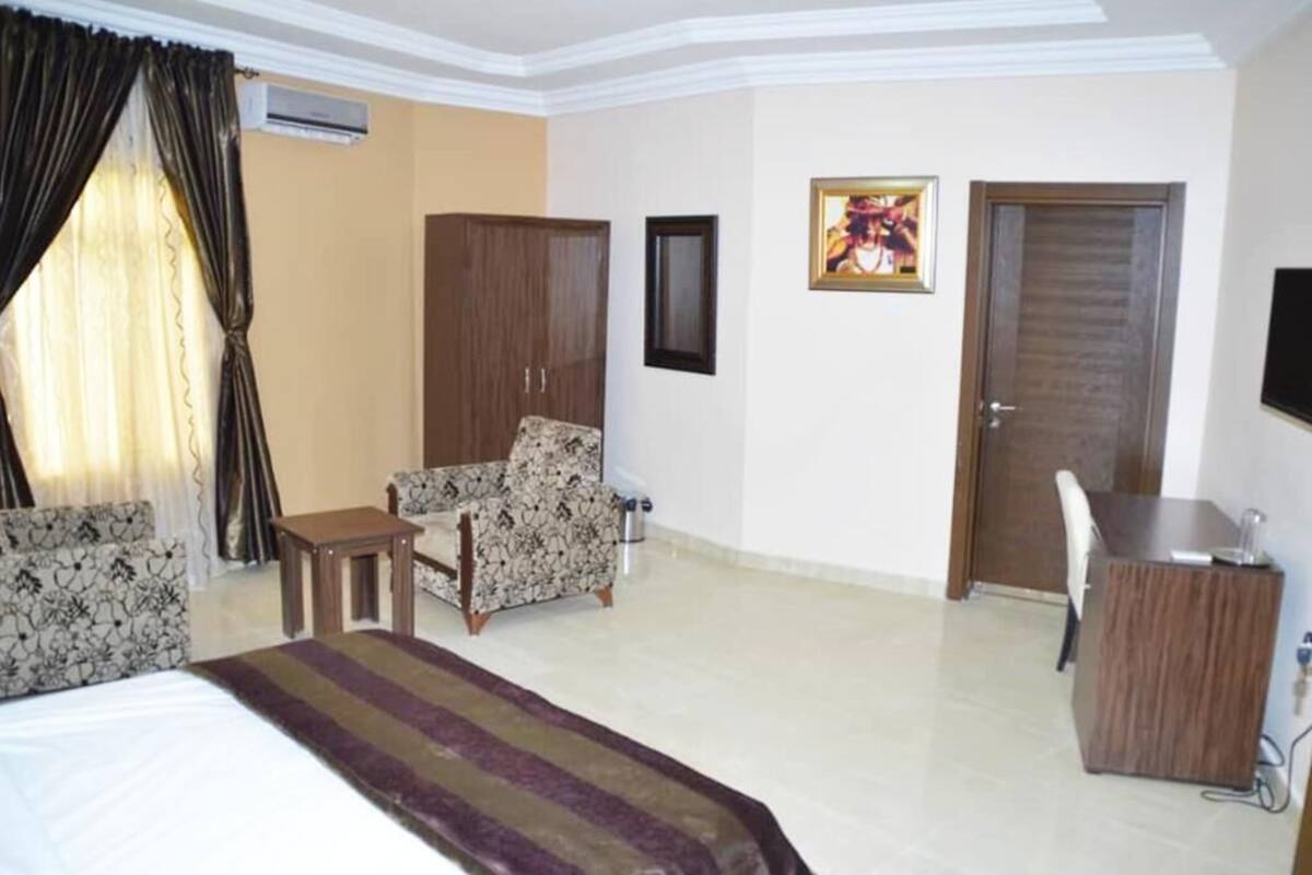 Une chambre d’hôtel avec un lit, un bureau, une chaise, une armoire et une porte.