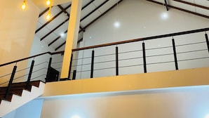 A multi-level interior with exposed wooden beams, a staircase with black railings, and hanging light fixtures. - Sigiri Holiday Bungalow (Sigiriya)