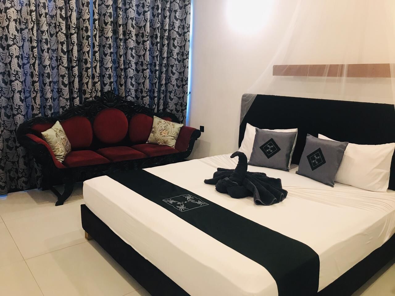 A hotel room with a large bed, a red sofa, and patterned curtains.
