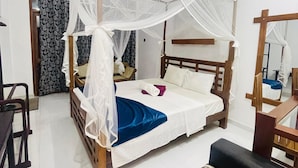 A room with a bed under a canopy, a wooden headboard, a bedside table, a chair, and a striped sofa. - Sigiri Holiday Bungalow (Sigiriya)