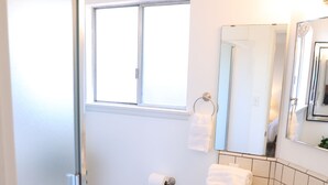 Une salle de bain avec une porte de douche en verre, des toilettes, un lavabo avec un miroir et une fenêtre au-dessus du lavabo.