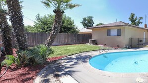 Un jardin avec une piscine, une clôture en bois et une maison équipée d’une antenne parabolique.