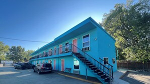 Un bâtiment à deux étages, avec une façade bleue, un escalier et un parking où sont garées des voitures.
