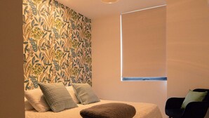A modern bedroom with a patterned wallpaper, a bed with pillows, a hanging light fixture, and a window with blinds. - Beautiful Loft in a brand new Condo, 10 minutes from business center.  (Santa Cruz de la Sierra)