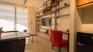 A modern living room with a glass coffee table, a red chair, a TV mounted on a wooden shelf, and a black refrigerator. - Beautiful Loft in a brand new Condo, 10 minutes from business center.  (Santa Cruz de la Sierra)
