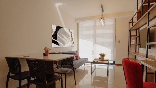 A modern living room with a dining area, a sofa, a red chair, a coffee table, and a bookshelf. - Beautiful Loft in a brand new Condo, 10 minutes from business center.  (Santa Cruz de la Sierra)