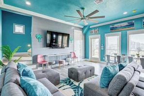 A modern living room with a teal accent wall, a ceiling fan, and a flat-screen TV mounted above a fireplace.