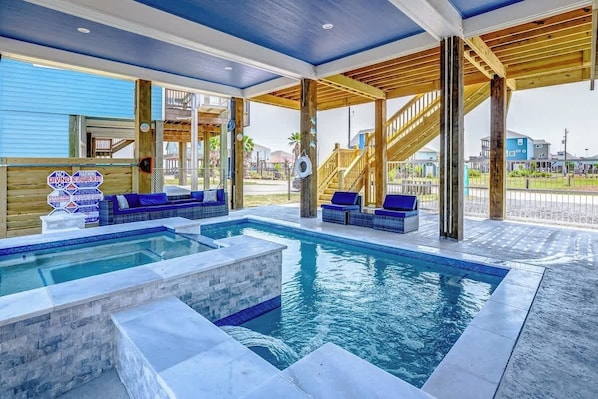 A pool area with blue lounge chairs, a wooden deck, and a view of the surrounding neighborhood.