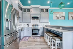 A modern kitchen with stainless steel appliances, light gray cabinets, and a teal accent wall.