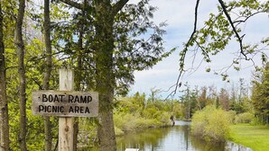 Un poste de madera con el texto 'Boat Ramp Picnic Area', un camino de hormigón, un pequeño embarcadero y una masa de agua tranquila rodeada de árboles.