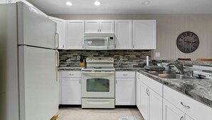 Una cocina moderna con armarios blancos, microondas integrado, estufa y pileta.