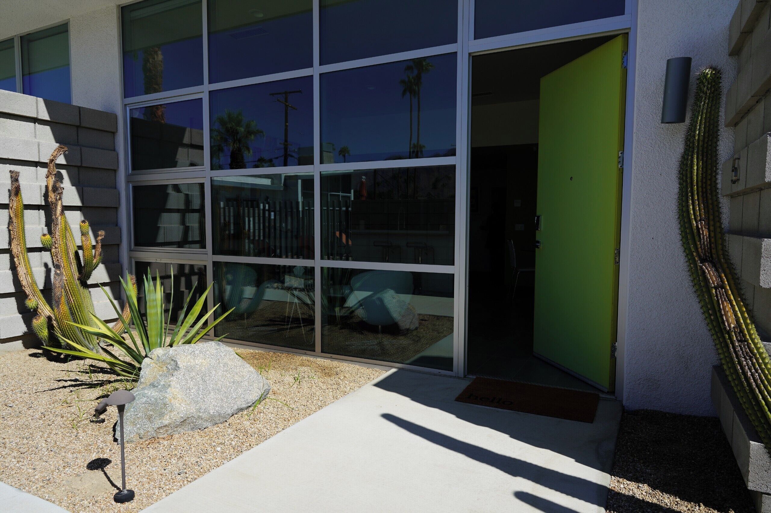 Un edificio moderno con ventanas amplias, una puerta verde y un cactus al frente.