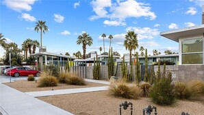 Un edificio moderno con fachada de vidrio, rodeado de paisaje desértico que incluye cactus y palmeras.