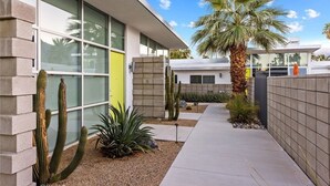 Un edificio moderno con ventanas amplias, una palmera y cactus en primer plano.