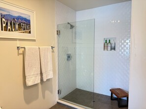 A bathroom with a glass shower enclosure, white tiled walls, a framed picture of Palm Springs, and a small bench. - Mid Century Vibes close to Downtown Palm Springs (Palm Springs)